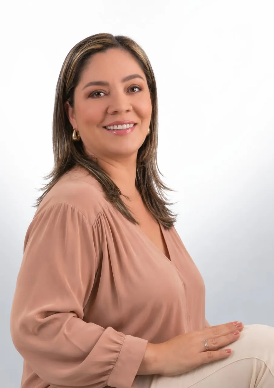 Mary Rivera, con una blusa rosa empolvado, sonriendo de lado.
