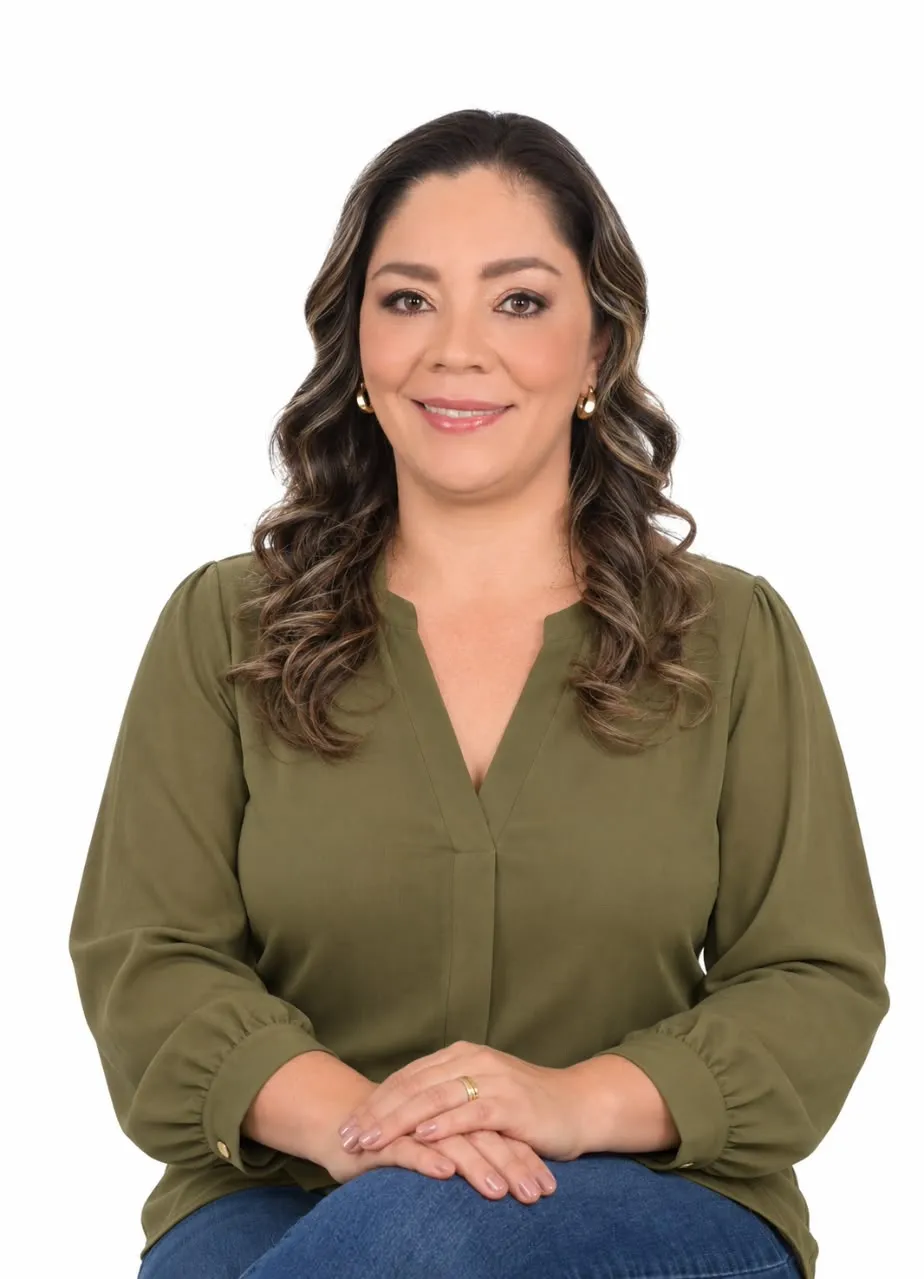 Mary Rivera, con una blusa verde oliva, mirando a cámara con las manos juntas.